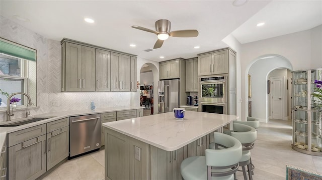 kitchen with a center island, gray cabinets, appliances with stainless steel finishes, arched walkways, and a sink