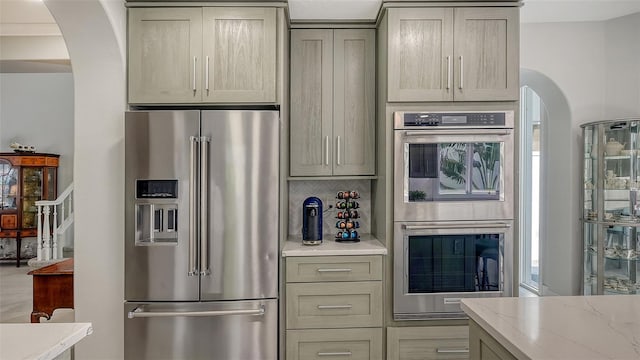 kitchen featuring arched walkways, backsplash, appliances with stainless steel finishes, and light stone countertops