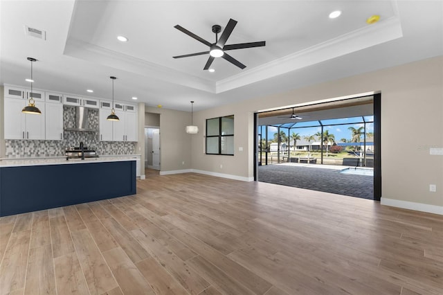 unfurnished living room with ceiling fan, light wood-style floors, crown molding, and a raised ceiling