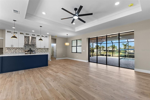 unfurnished living room with visible vents, ceiling fan, ornamental molding, light wood-style floors, and a tray ceiling