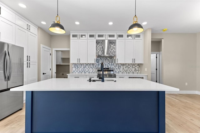 kitchen with tasteful backsplash, a sink, light wood-style floors, freestanding refrigerator, and wall chimney exhaust hood