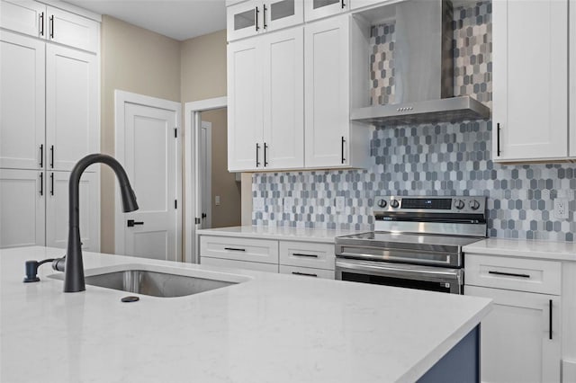 kitchen featuring stainless steel electric stove, backsplash, a sink, wall chimney range hood, and white cabinets
