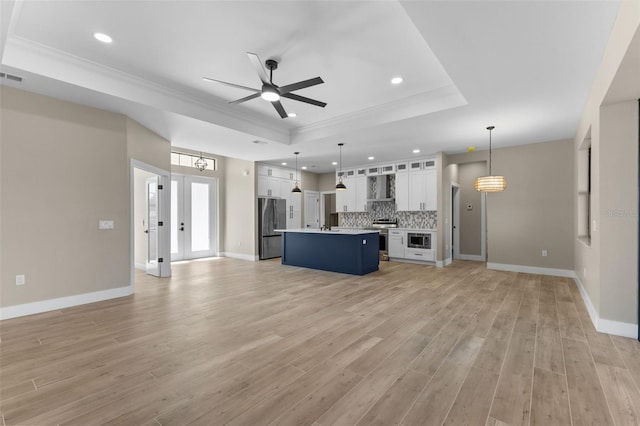 unfurnished living room featuring light wood-type flooring, a ceiling fan, ornamental molding, and a raised ceiling