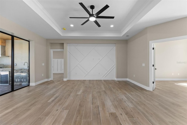 unfurnished living room featuring crown molding, light wood finished floors, baseboards, ceiling fan, and a tray ceiling