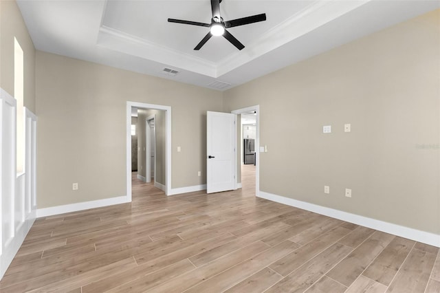 empty room with a tray ceiling, baseboards, light wood-style floors, ceiling fan, and visible vents