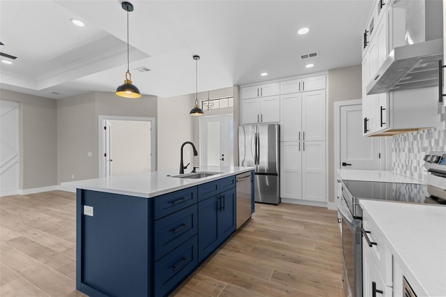 kitchen featuring a sink, blue cabinets, light wood-style flooring, stainless steel appliances, and wall chimney range hood