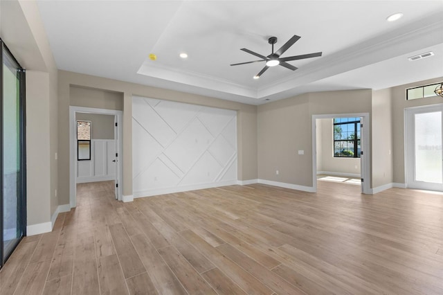 unfurnished living room featuring visible vents, light wood finished floors, baseboards, a ceiling fan, and a tray ceiling