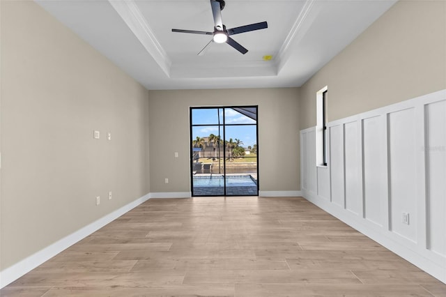 spare room featuring a tray ceiling, crown molding, baseboards, light wood-style floors, and a ceiling fan