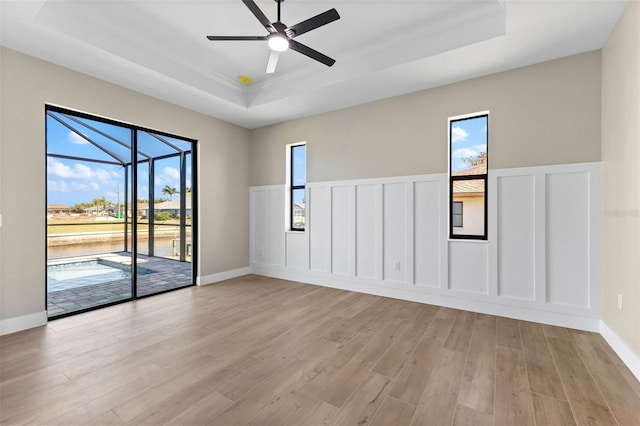spare room featuring a tray ceiling, a sunroom, a decorative wall, and a ceiling fan