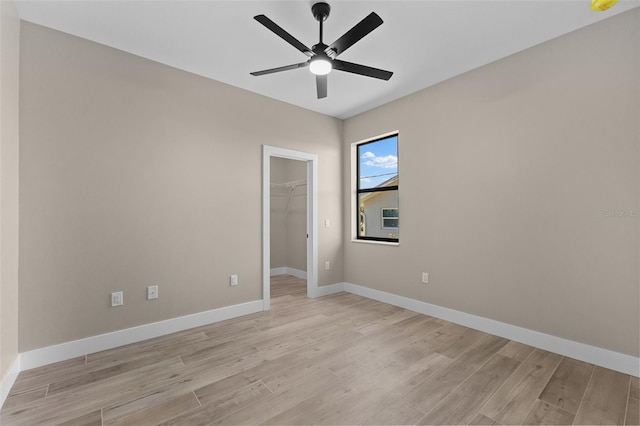unfurnished bedroom with a spacious closet, a ceiling fan, baseboards, and light wood-type flooring