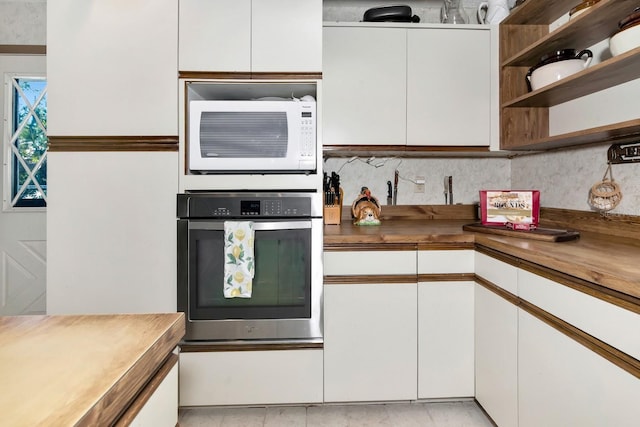 2070 59th St, Sarasota, FL 34243 - kitchen with stainless steel oven, white microwave, open shelves, wood counters, and white cabinets