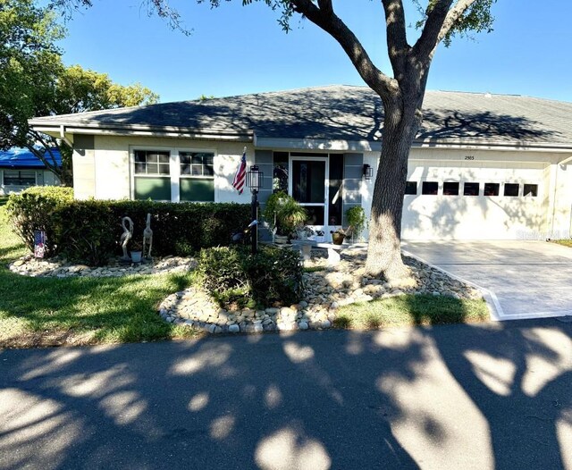 ranch-style home featuring a garage, roof with shingles, concrete driveway, and stucco siding
