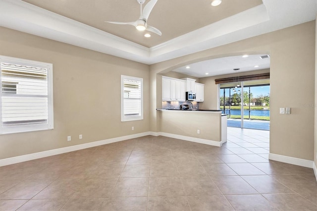 interior space featuring stainless steel microwave, a tray ceiling, recessed lighting, and light tile patterned flooring