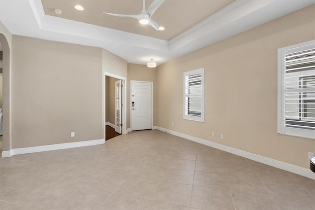 spare room with ceiling fan, arched walkways, light tile patterned floors, baseboards, and a tray ceiling