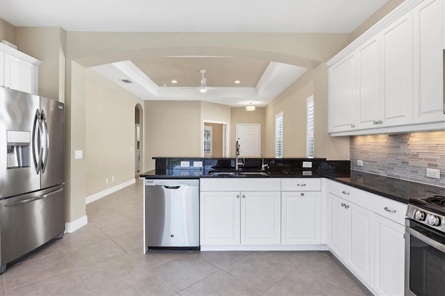 kitchen featuring decorative backsplash, arched walkways, a sink, a peninsula, and stainless steel appliances
