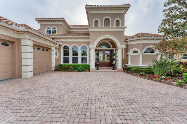 mediterranean / spanish-style home featuring a tiled roof, an attached garage, stucco siding, french doors, and decorative driveway