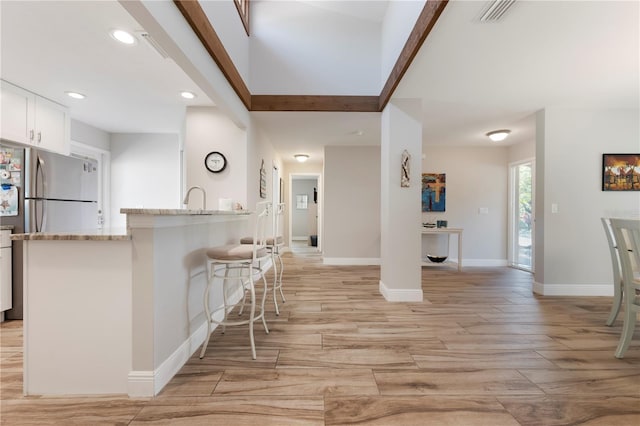 3804 Sun Eagle Ln, Bradenton, FL 34210 - kitchen with a breakfast bar area, light stone counters, light wood finished floors, visible vents, and white cabinets