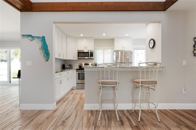 3804 Sun Eagle Ln, Bradenton, FL 34210 - kitchen with backsplash, light wood finished floors, white cabinetry, a breakfast bar, and stainless steel appliances