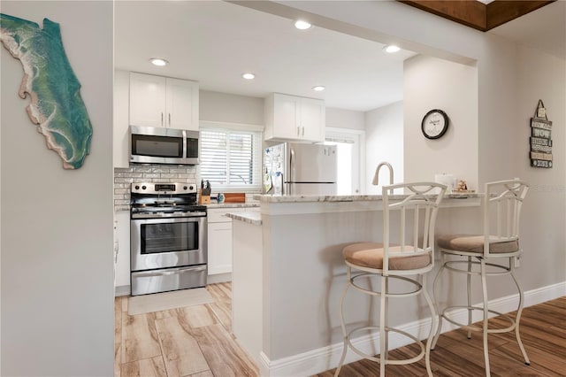 3804 Sun Eagle Ln, Bradenton, FL 34210 - kitchen featuring light stone counters, a breakfast bar, stainless steel appliances, white cabinets, and light wood-style floors