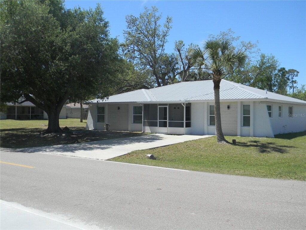 single story home featuring driveway, a sunroom, a front lawn, and metal roof
