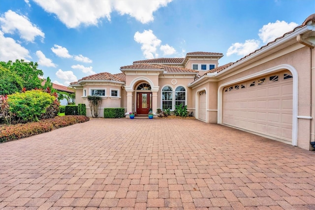 mediterranean / spanish home featuring a tile roof, an attached garage, decorative driveway, and stucco siding