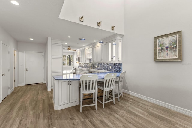 1928 Harbourside Dr Unit 1403, Longboat Key, FL 34228 - kitchen featuring light wood finished floors, baseboards, white cabinets, a peninsula, and stainless steel microwave