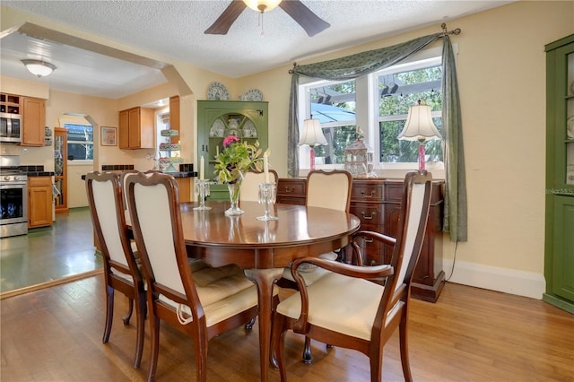 dining room with baseboards, arched walkways, ceiling fan, a textured ceiling, and light wood-type flooring