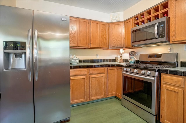 kitchen featuring brown cabinetry, light wood-style flooring, stainless steel appliances, and tile counters