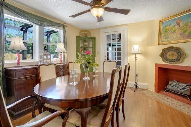 dining room featuring light wood-style flooring, a fireplace with flush hearth, a ceiling fan, and a textured ceiling
