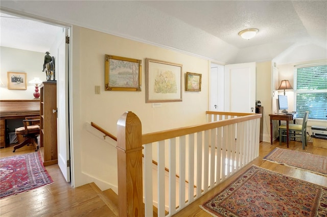 corridor with wood finished floors, an upstairs landing, lofted ceiling, and a textured ceiling
