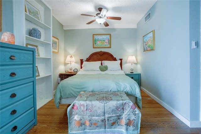 bedroom with visible vents, a ceiling fan, a textured ceiling, wood finished floors, and baseboards