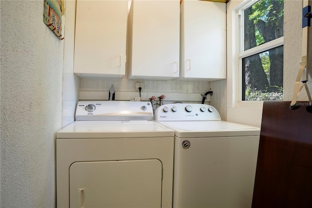 clothes washing area with a textured wall, cabinet space, and washer and clothes dryer