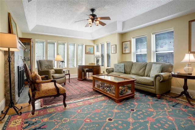 living area featuring a raised ceiling, a ceiling fan, baseboards, and a healthy amount of sunlight