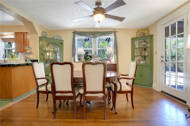dining area featuring arched walkways, light wood-style floors, ceiling fan, and a textured ceiling