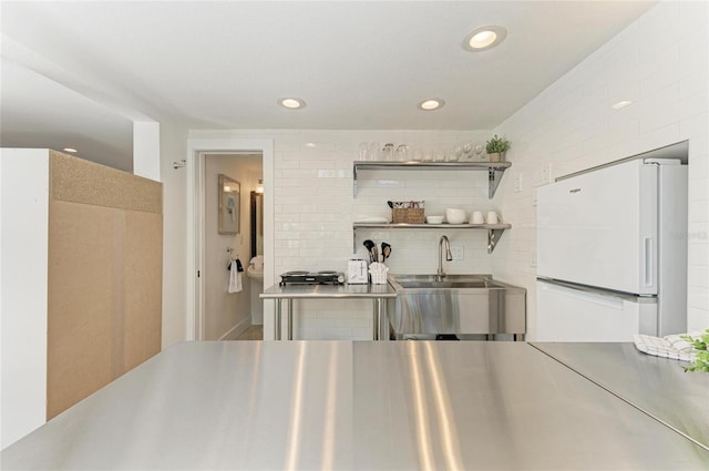 kitchen with open shelves, freestanding refrigerator, a sink, stainless steel counters, and tasteful backsplash