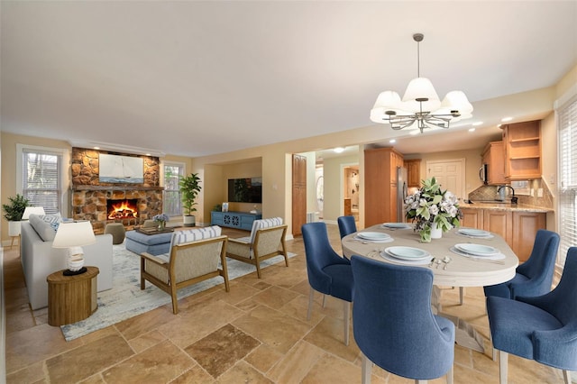 dining space featuring a notable chandelier, a healthy amount of sunlight, a fireplace, and stone tile floors