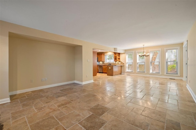 unfurnished living room with baseboards, a chandelier, and stone tile flooring