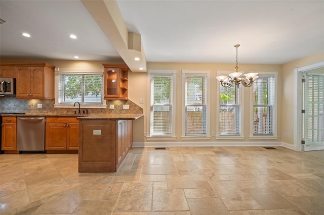 kitchen with brown cabinetry, tasteful backsplash, stone tile floors, a chandelier, and appliances with stainless steel finishes