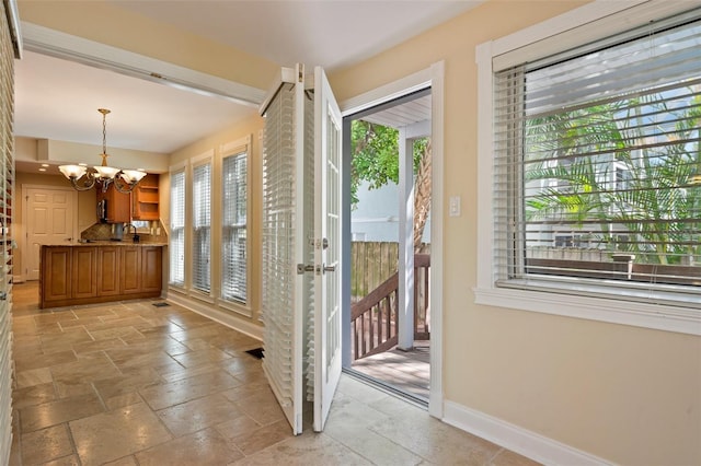 doorway featuring stone tile floors, a notable chandelier, and baseboards