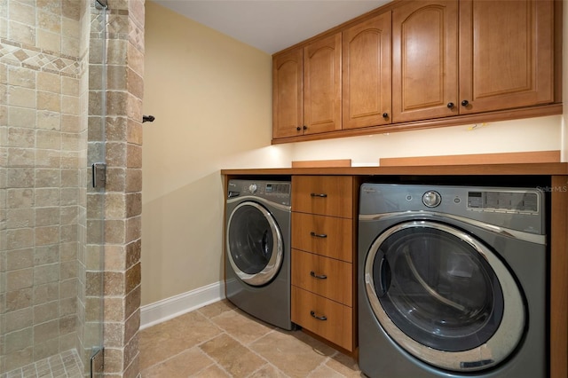 clothes washing area with baseboards, stone finish flooring, separate washer and dryer, and cabinet space