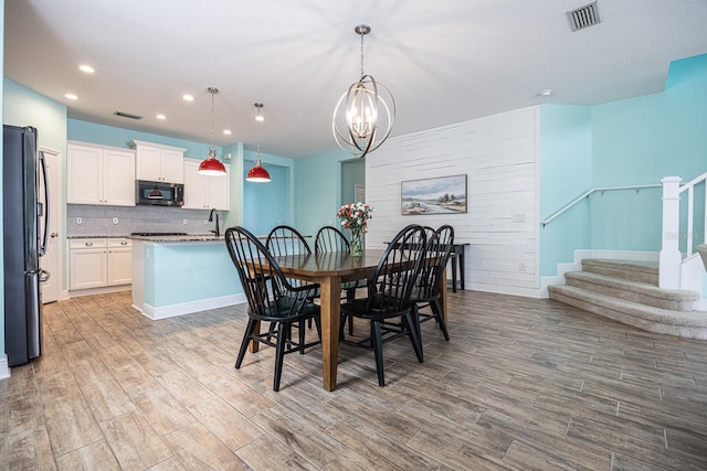 dining space featuring wood finished floors, visible vents, stairs, and a notable chandelier