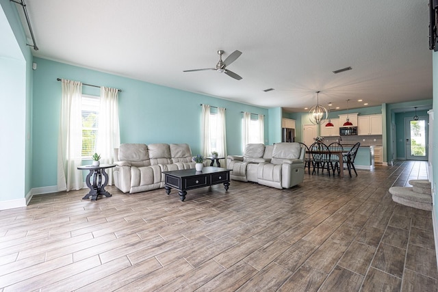 living room with ceiling fan with notable chandelier, baseboards, visible vents, and dark wood-style flooring