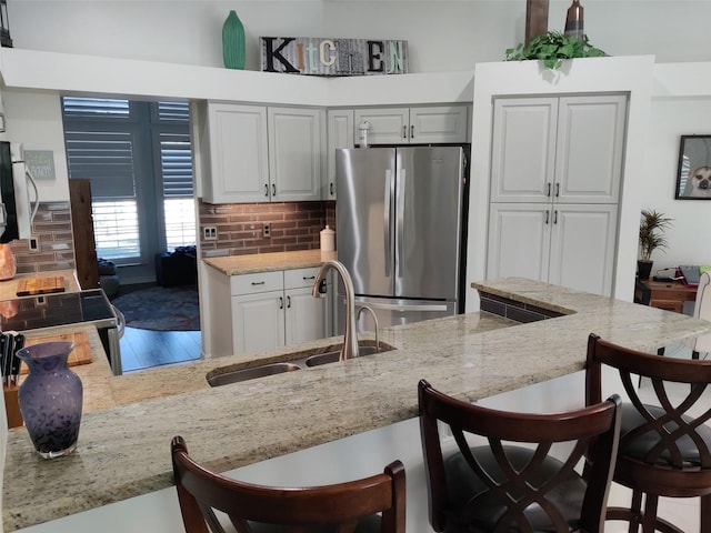 1118 Deardon Dr, Venice, FL 34292 - kitchen featuring a kitchen bar, tasteful backsplash, a sink, light stone counters, and freestanding refrigerator