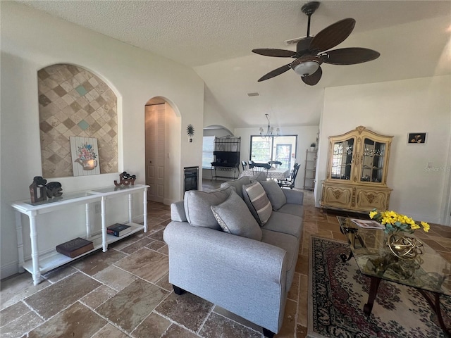 living room with lofted ceiling, a textured ceiling, arched walkways, ceiling fan, and stone tile flooring