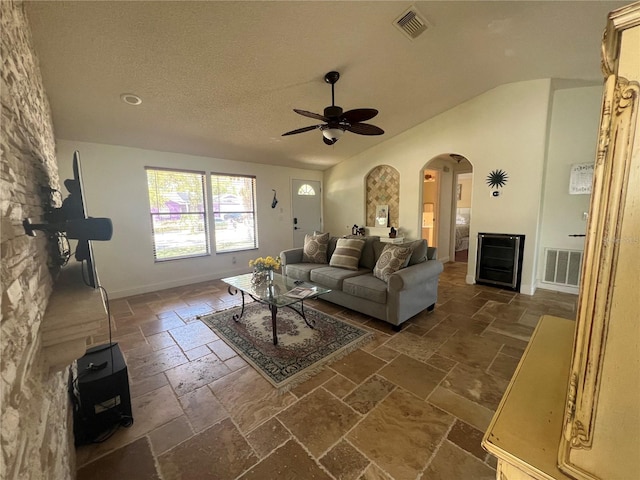 living room featuring visible vents, stone tile floors, arched walkways, and a ceiling fan