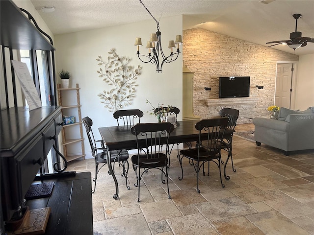 dining space featuring ceiling fan with notable chandelier, lofted ceiling, stone tile floors, and a textured ceiling