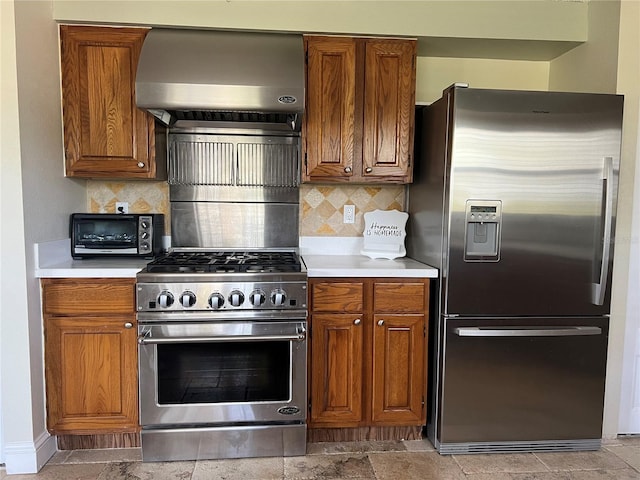 kitchen with light countertops, wall chimney exhaust hood, brown cabinets, stainless steel appliances, and a toaster