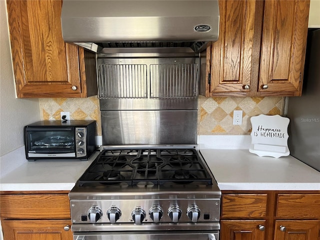 kitchen featuring stainless steel stove, backsplash, wall chimney range hood, and brown cabinetry
