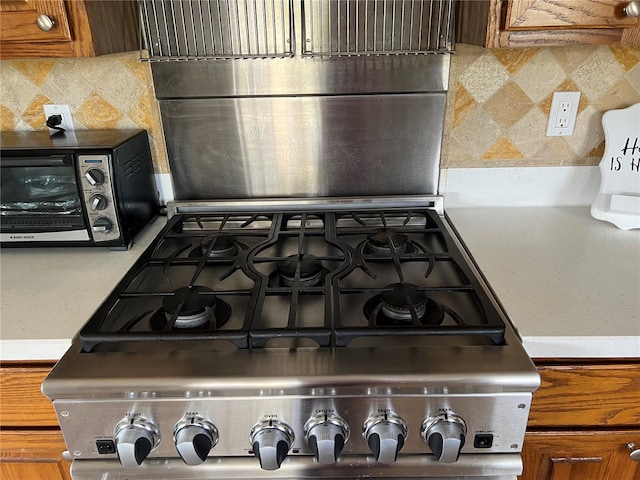 details with range, light countertops, a toaster, brown cabinets, and backsplash