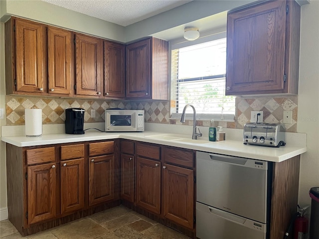 kitchen with a textured ceiling, light countertops, a sink, white microwave, and stainless steel dishwasher